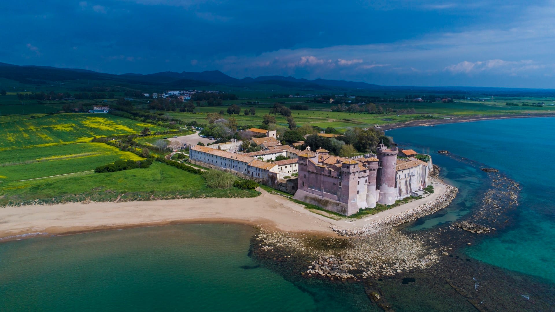 A beach with clear turquois waters and a castle at the end of the beach.