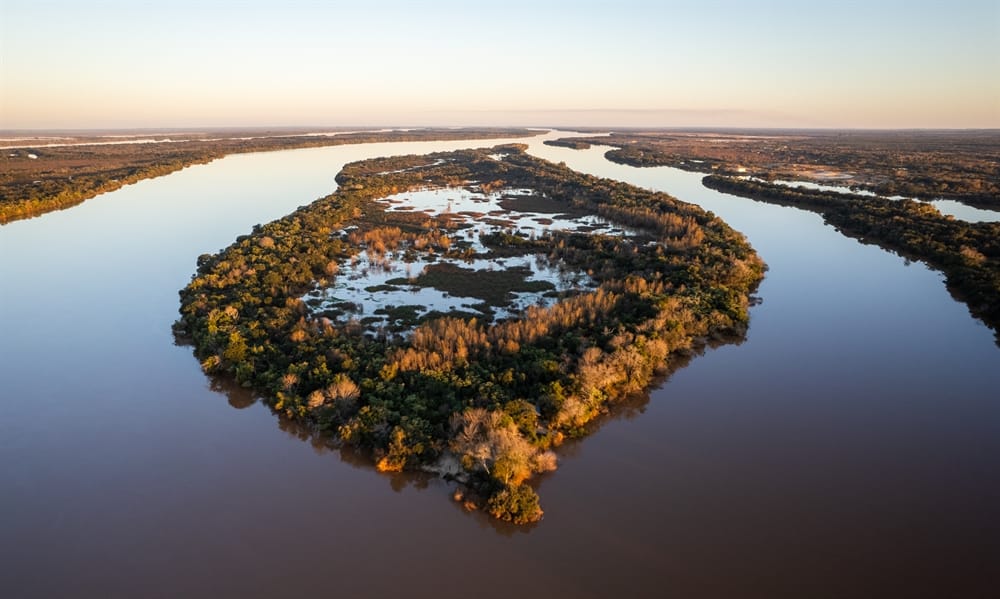 Aerial view of lush green islands and wetlands surrounded by wide river channels at Esteros de Farrapos National Park in Uruguay, during a calm, golden sunset.