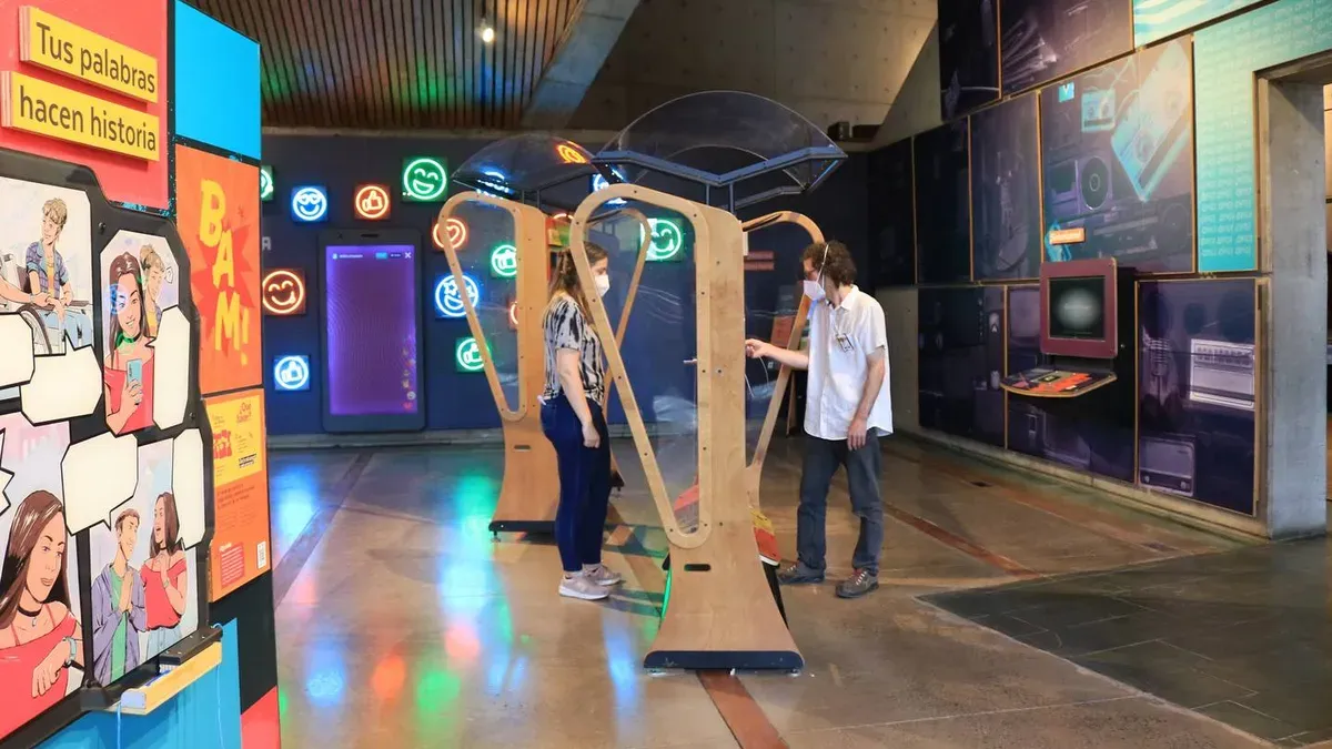 Interactive exhibit at the Mirador Museum (MIM) with two people engaging with wooden structures, colorful lights, and comic-style displays.