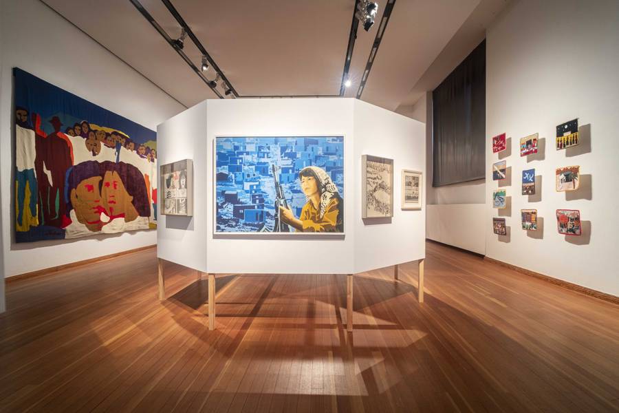 Art exhibit at Salvador Allende Museum featuring political artworks, including a central portrait of a woman with a rifle and colorful textiles.