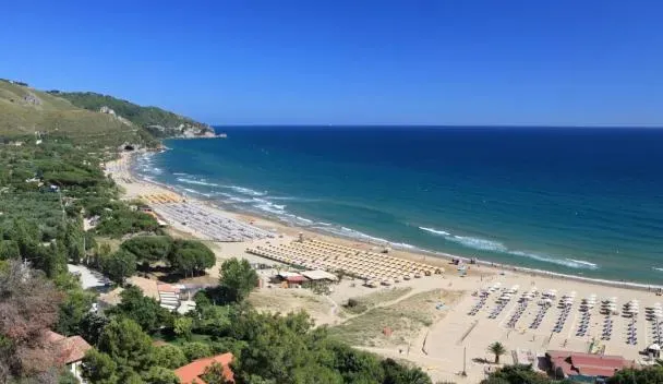 Ariel view of Sperlonga Beach, with waves washing onto a beach with lots of white beach chairs.