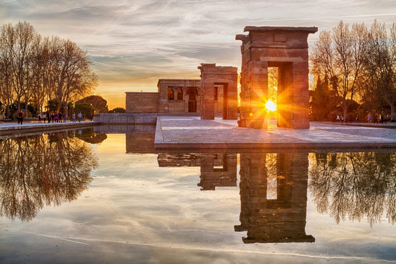 Sunset at the Templo de Debod in Madrid, Spain, with golden light shining through ancient stone arches and reflecting in the water.