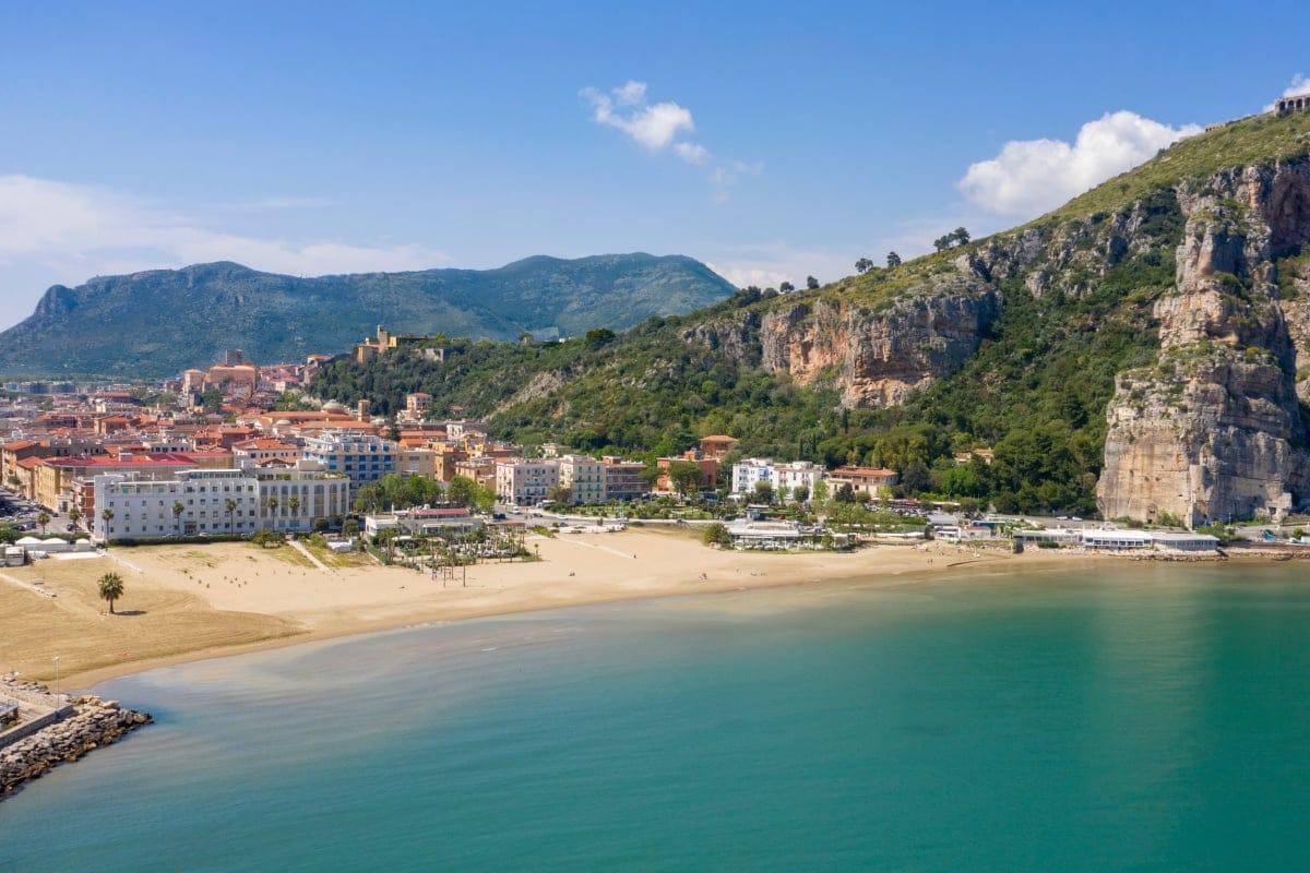 Ariel view of a beach that has a few resort buildings on it with mountains at one end of the beach.