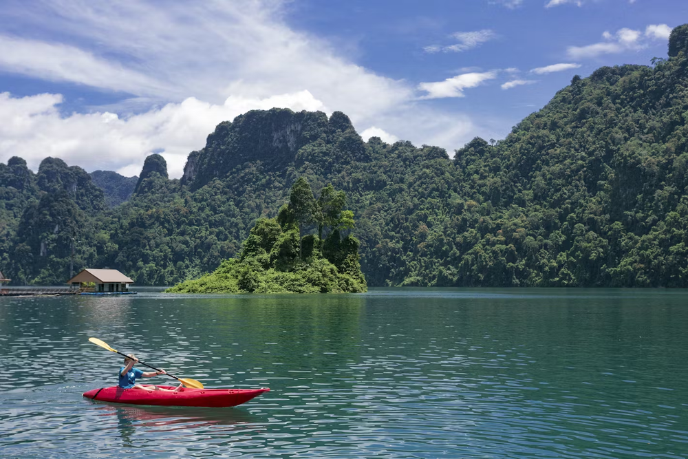 A person kayaking in a red kayak on a lake surrounded by mountains covered in lush jungle.