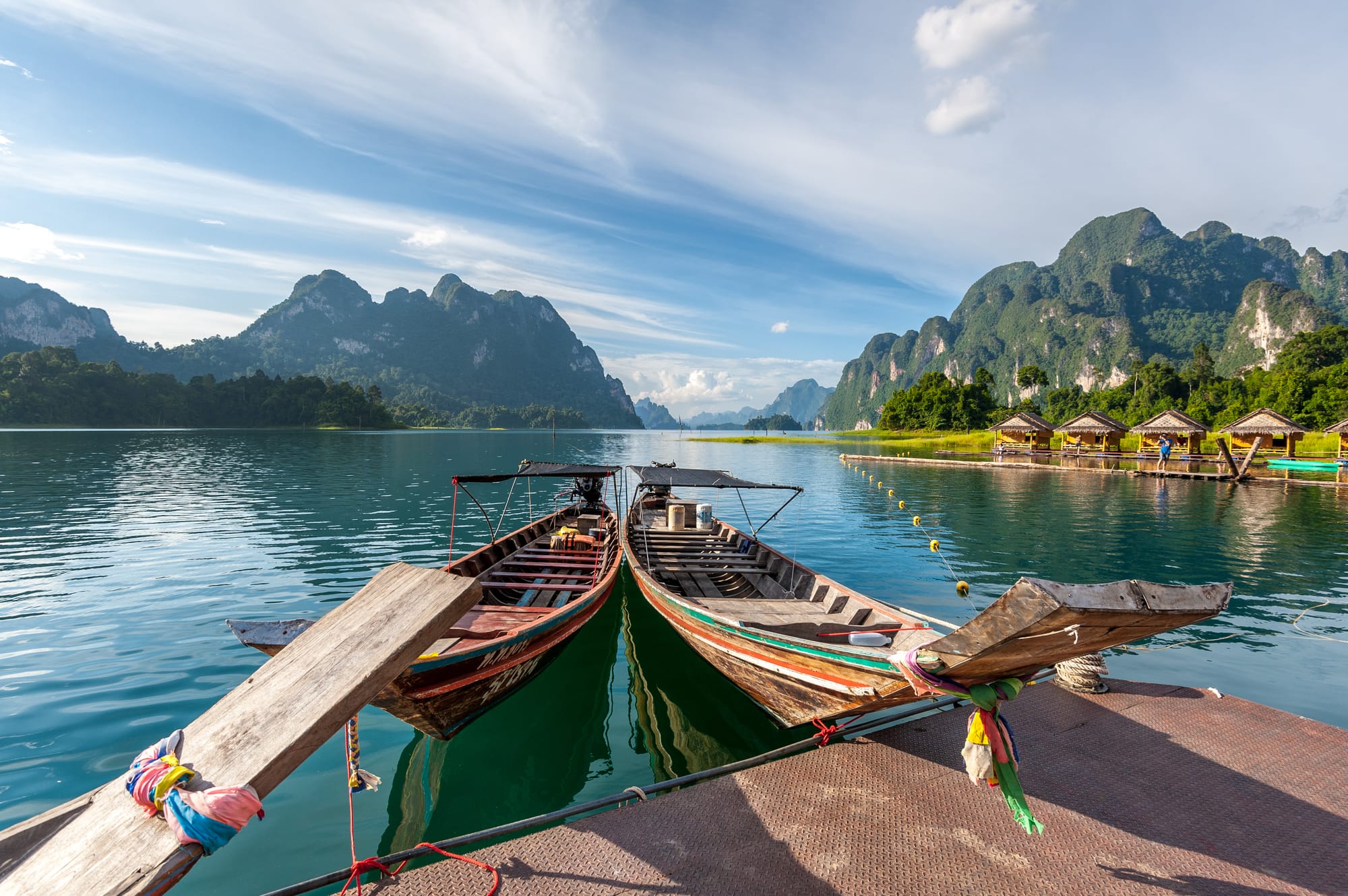 Two Thai stye long tail boats on a beautiful lake that is surrounded by a mountainous jungle.