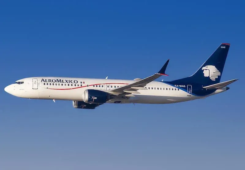 Aeromexico airplane in mid-flight against a clear blue sky, viewed from the side during descent.