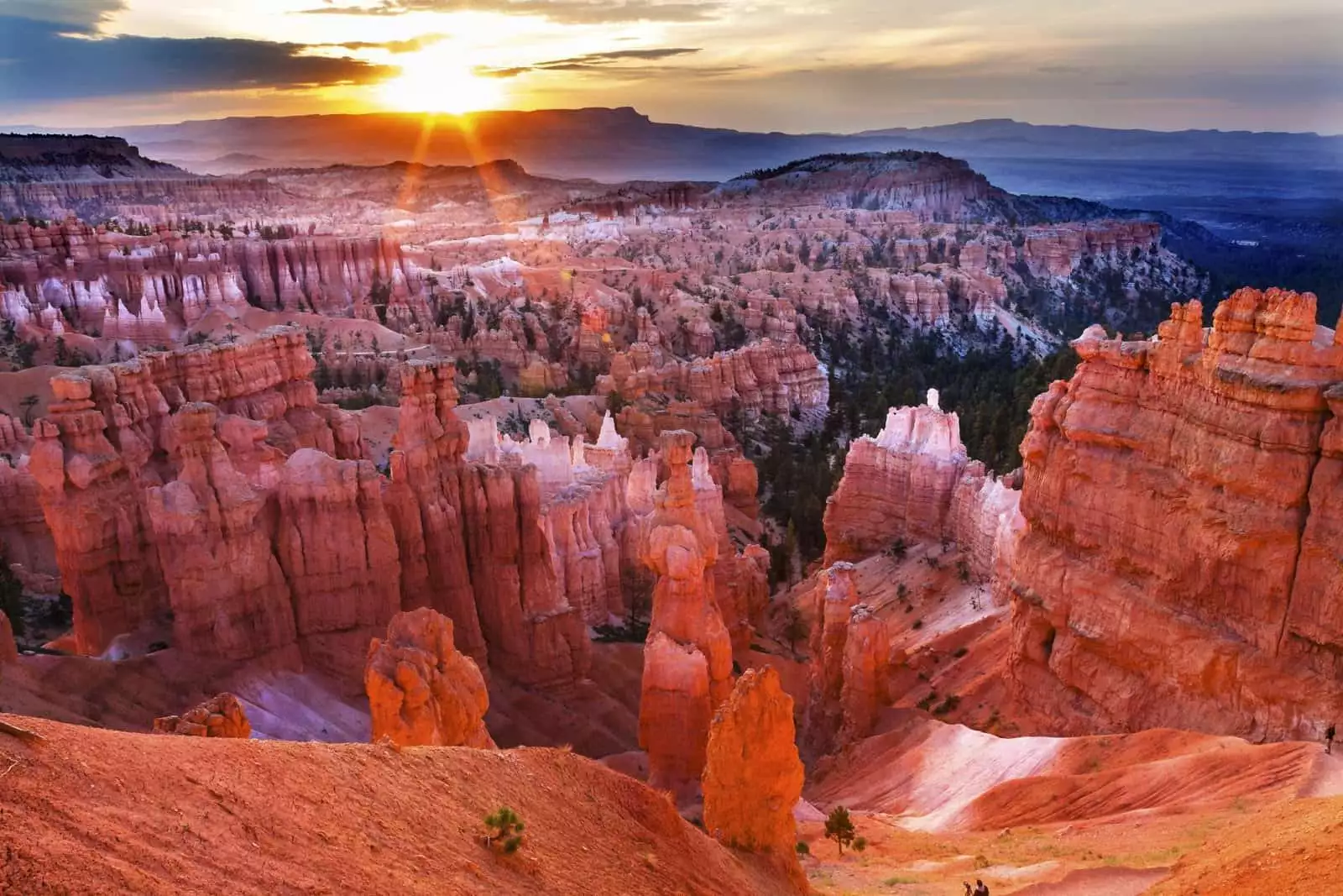 Sun rising over the red hoodoos and rock formations of Bryce Canyon National Park, casting light across the valley.