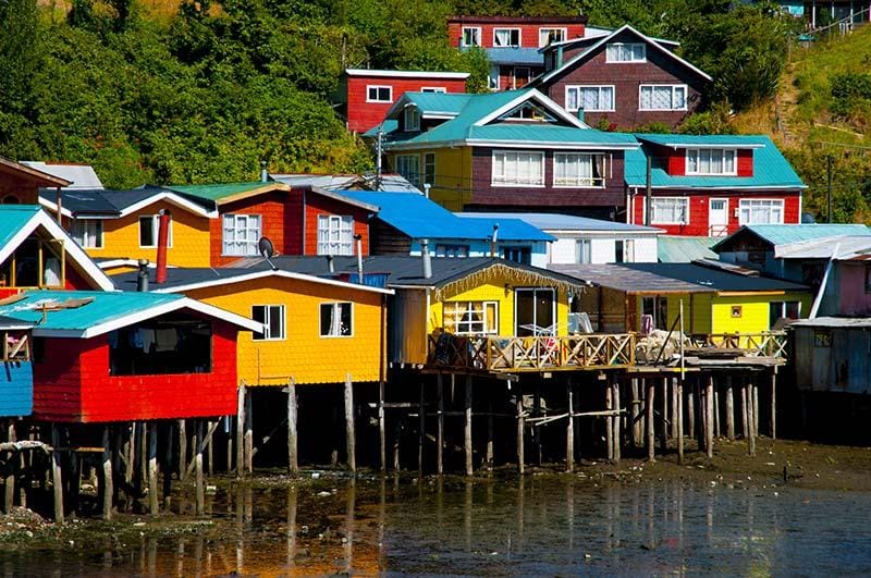Vibrant hillside view of colorful houses stacked along the slopes of Valparaíso, Chile, under a bright blue sky.