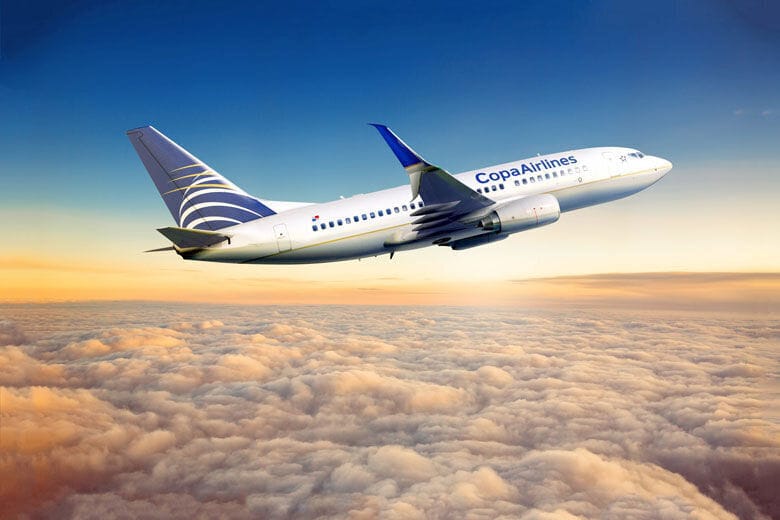 Copa Airlines airplane flying above the clouds during sunset, with warm orange and blue tones in the sky.
