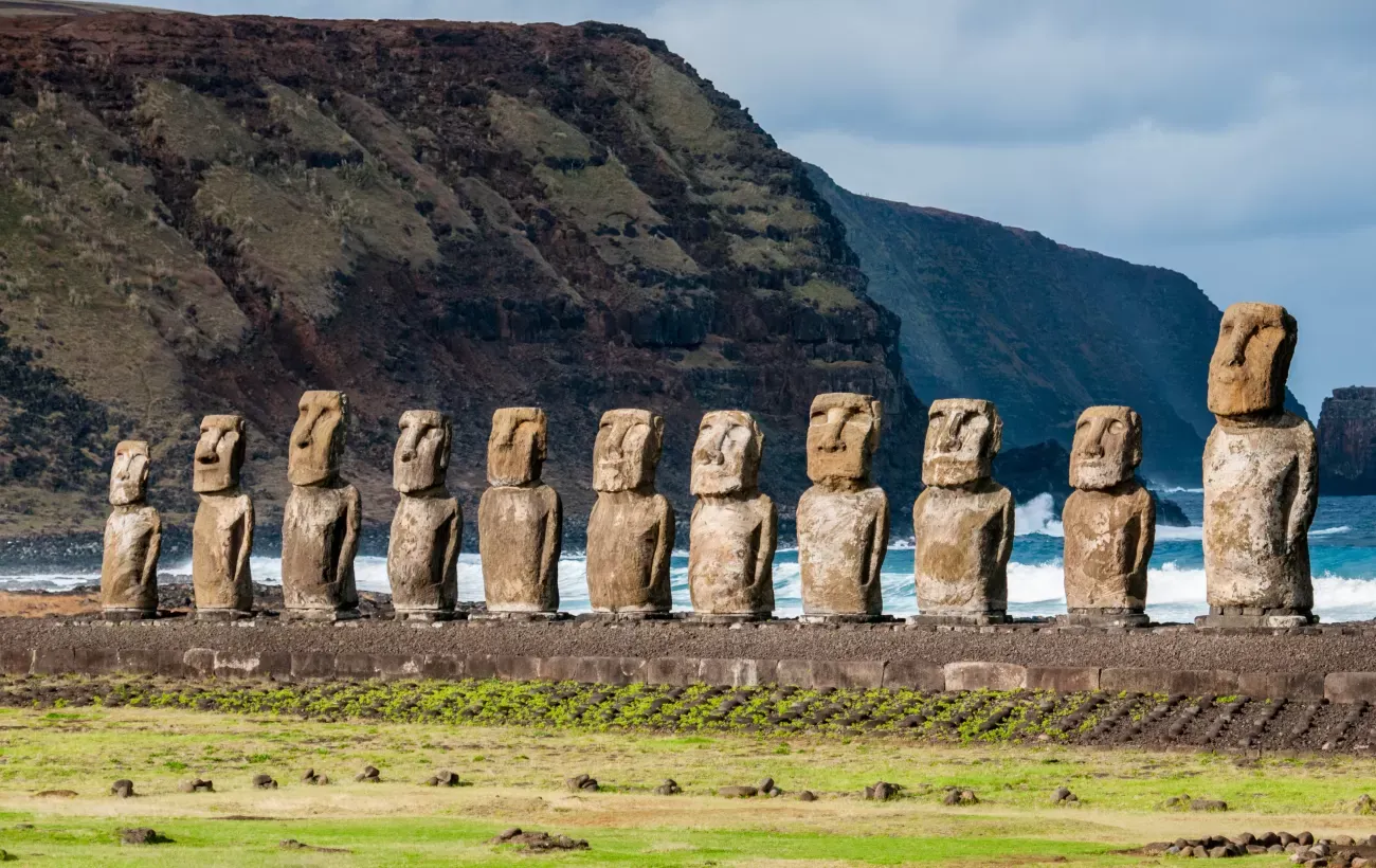 Moai statues at Ahu Tongariki on Easter Island, Chile, with ocean waves and rugged cliffs in the background.