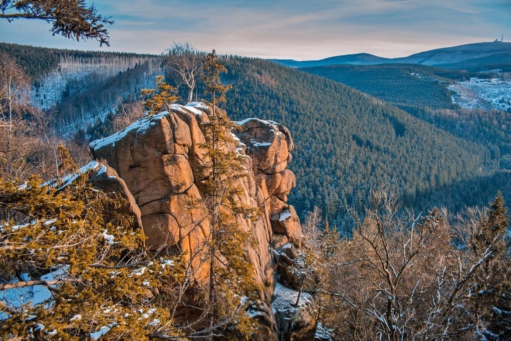 Snow-dusted rocky outcrop overlooking dense forested hills in Harz National Park, Germany, with a scenic winter landscape stretching into the distance.