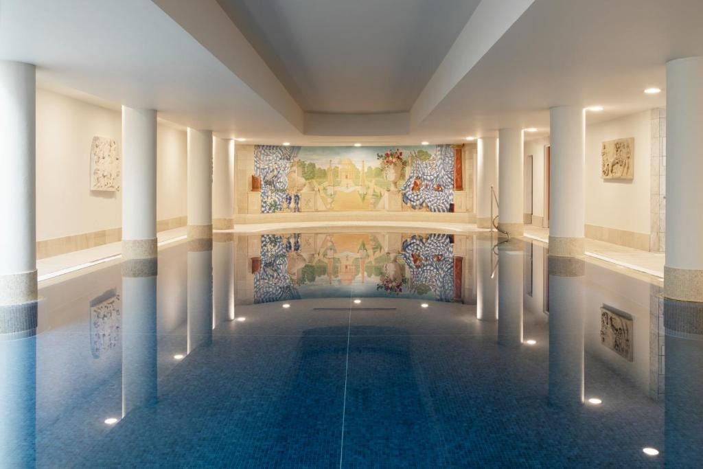 A beautiful and fancy indoor pool at the Merrion Hotel In Dublin with giant while columns going along the pool and large painting on the wall.