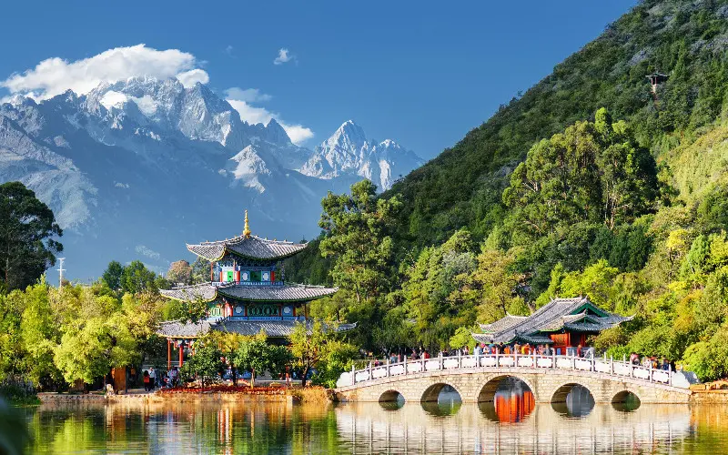 The Three Pagodas of Chongsheng Temple in Dali, Yunnan, China, reflected in a calm pond surrounded by lush greenery under a bright blue sky with scattered clouds.