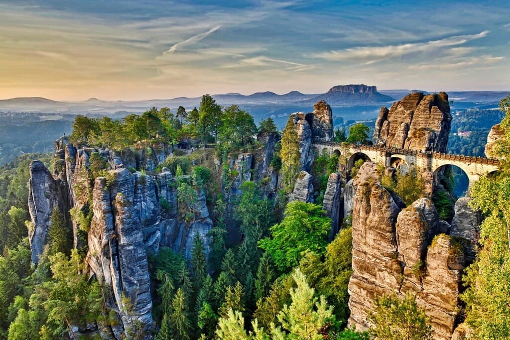 Iconic Bastei Bridge spanning towering sandstone rock formations amidst a forested valley in Saxon Switzerland National Park at sunrise