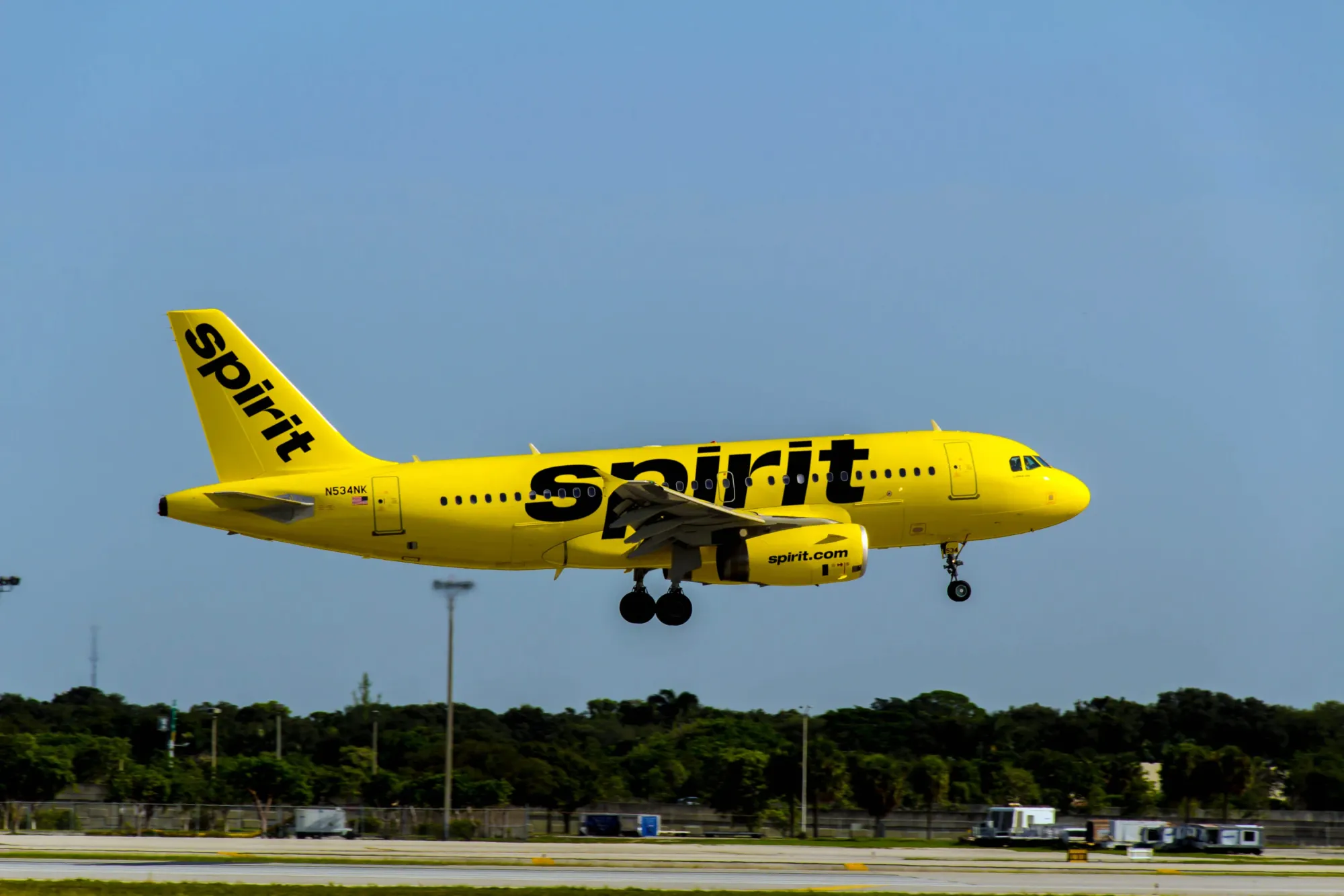 A bright yellow Spirit Airlines plane about to land on a runway with it's landing gear down.