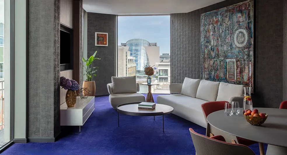 A luxury hotel suite with blue carpet and white living room furniture in a 1-bedroom suite at the Luxury Anantara The Marker Dublin hotel.
