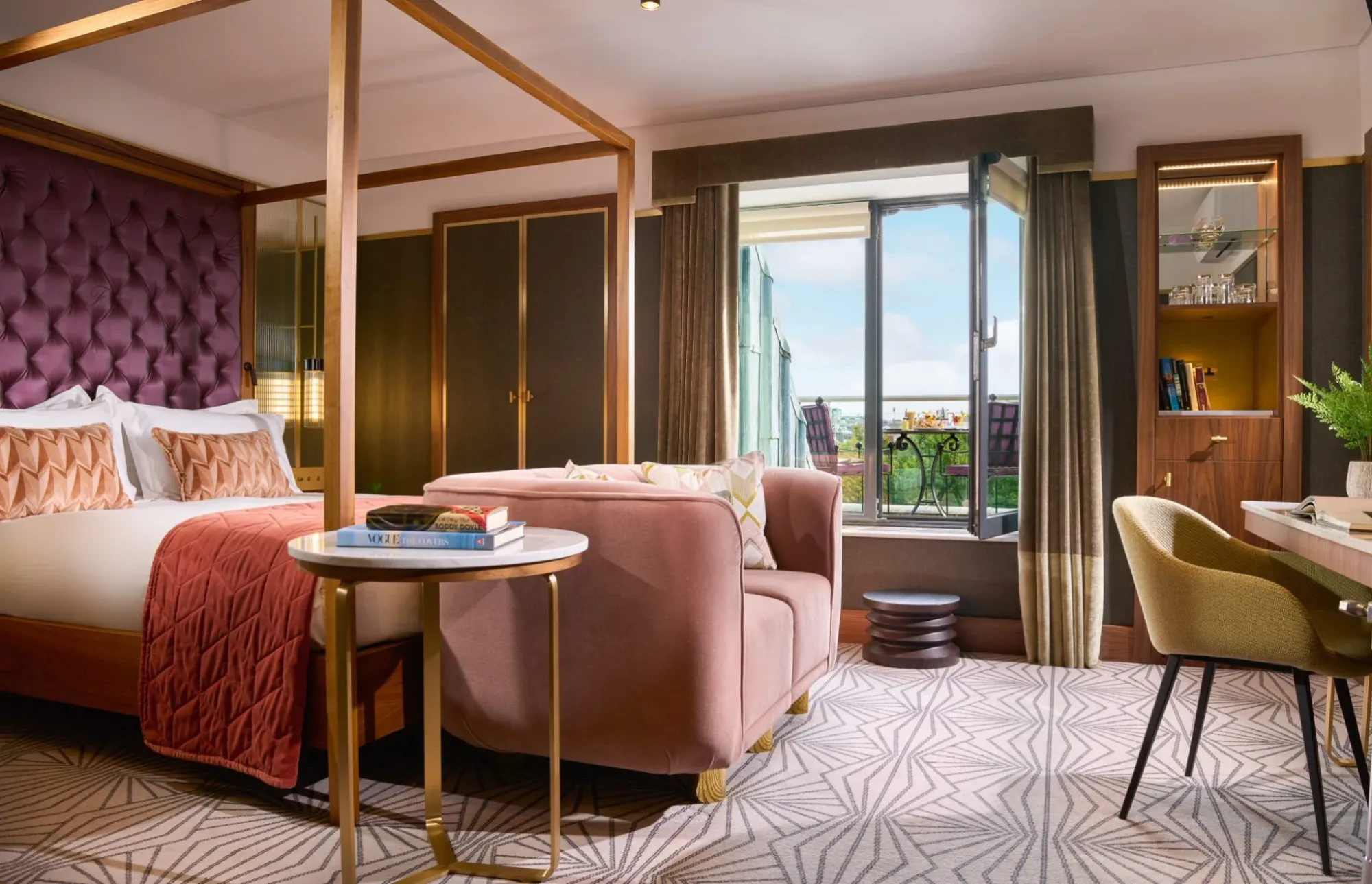 A luxury guest room at The Fitzwilliam Hotel in Dublin, showing a large 4-poster bed with a floor to ceiling purple leather headboard with a city view and balcony.