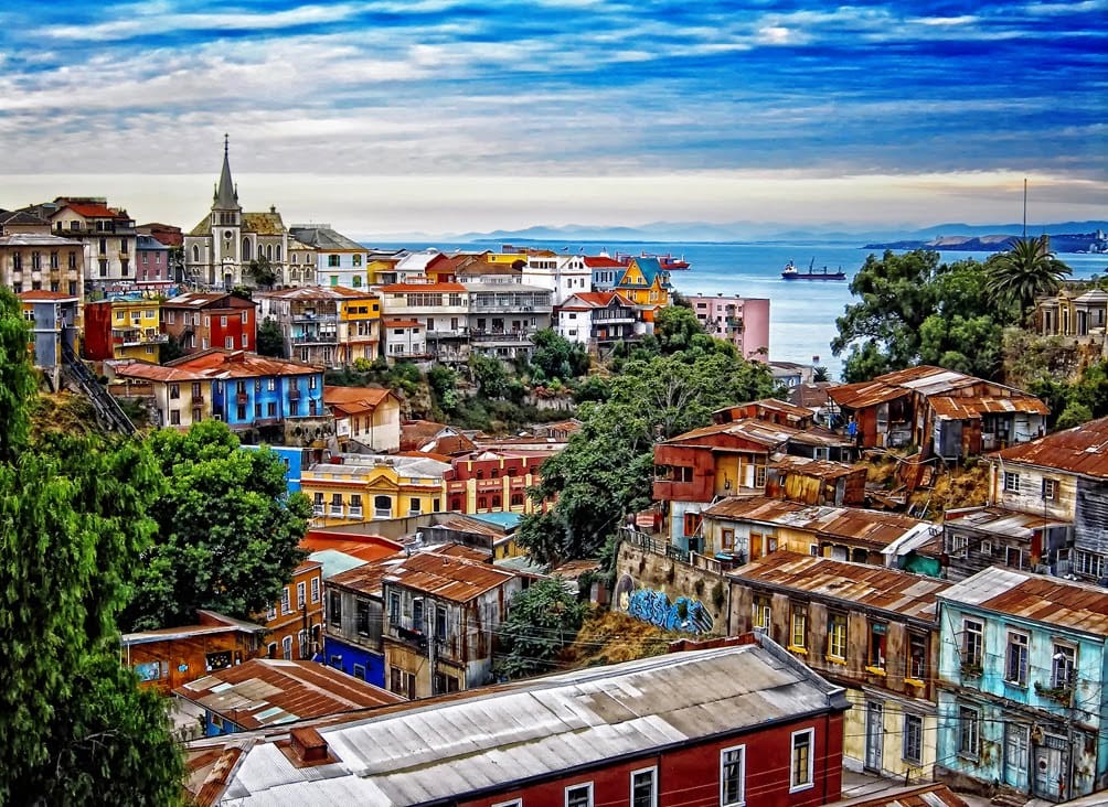 Colorful hillside houses and a church overlooking the Pacific Ocean in Valparaíso, Chile, with ships in the distant water.