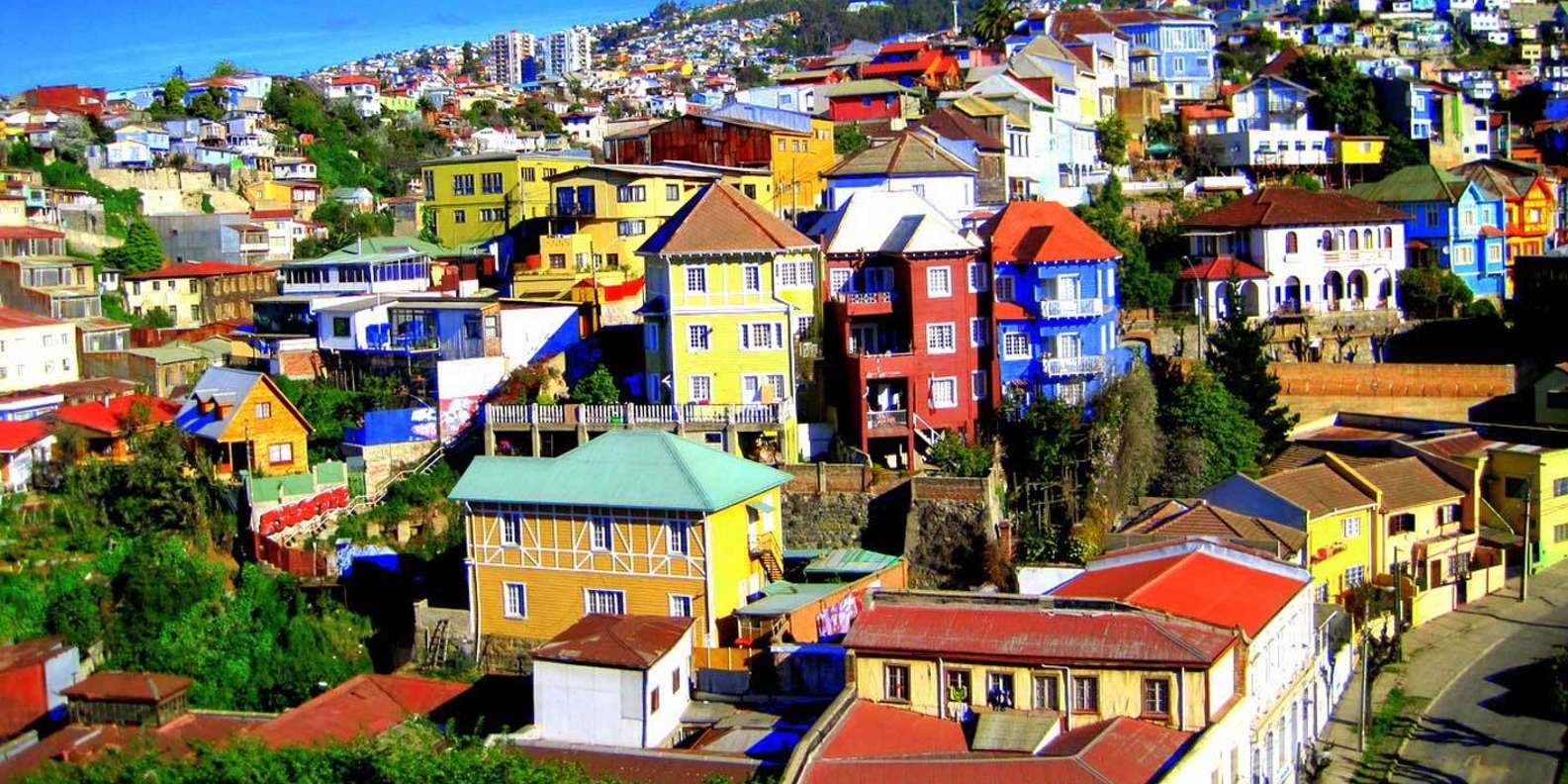 Vibrant hillside view of colorful houses stacked along the slopes of Valparaíso, Chile, under a bright blue sky.