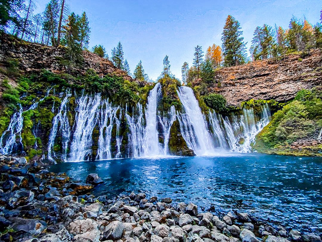 Burney Falls cascading over a mossy cliff into clear blue waters in Northern California.