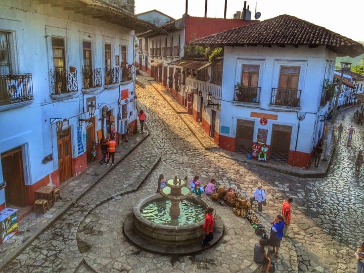 A view of Cuetzalan del Progreso, Mexico, featuring a historic stone church with a red dome and tiled roof surrounded by traditional homes with red rooftops.