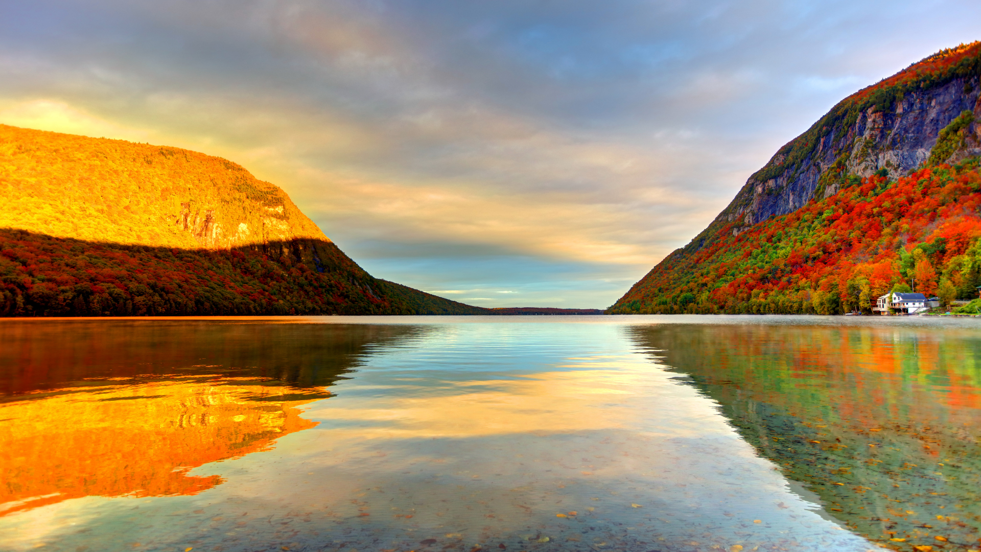 Fiery autumn colors surround peaceful Lake Willoughby at sunrise in Vermont.
