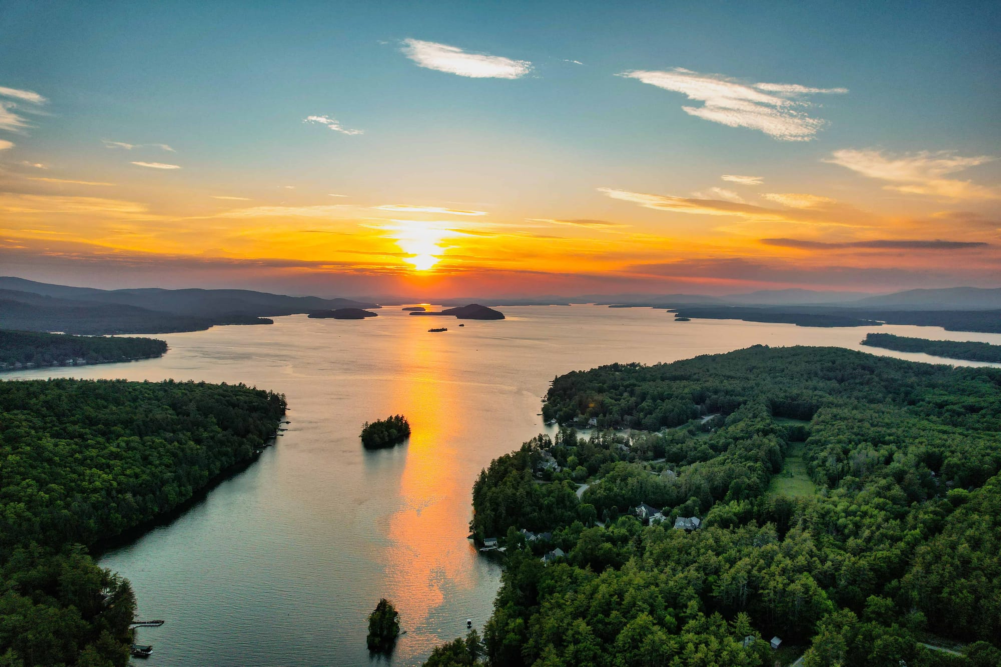 Sunset over Lake Winnipesaukee with forested islands and golden reflections across the calm water.