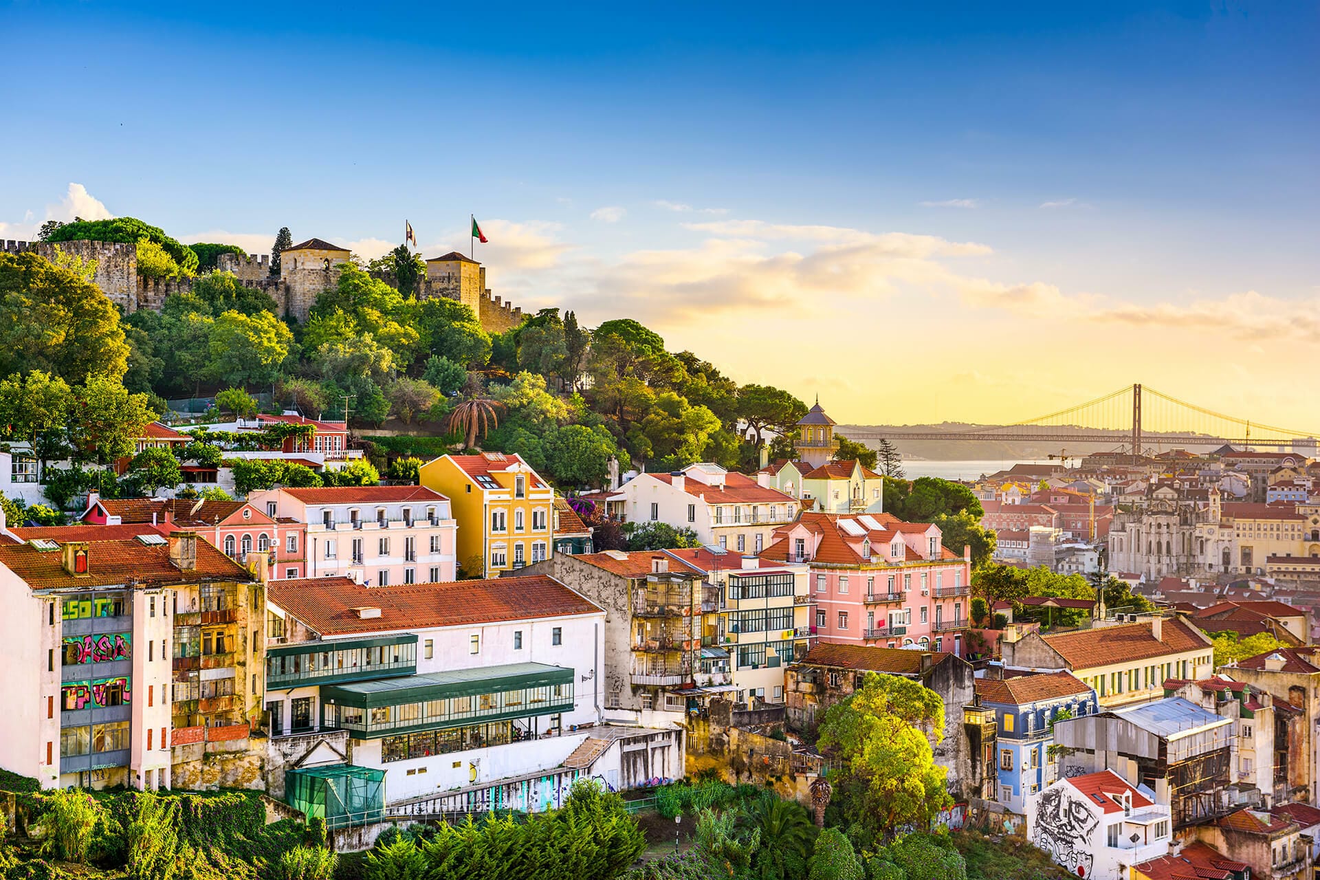 Colorful hillside buildings and São Jorge Castle overlook Lisbon at sunset.