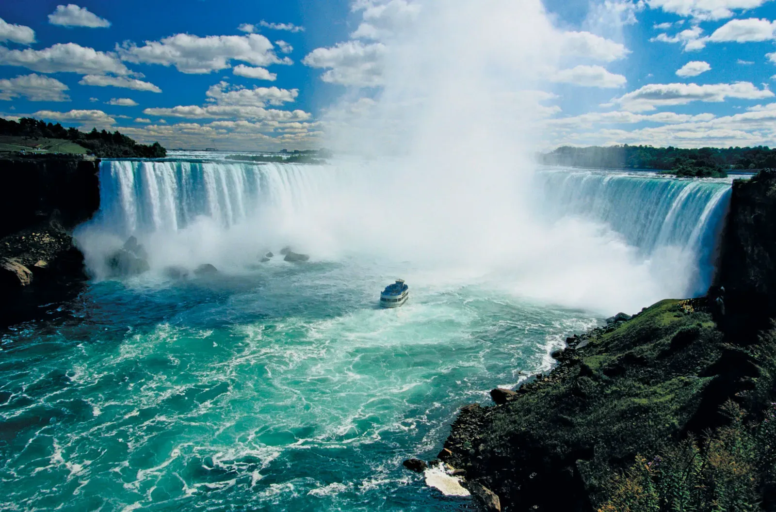 Massive Horseshoe Falls at Niagara Falls with mist rising and the Maid of the Mist boat entering the spray.