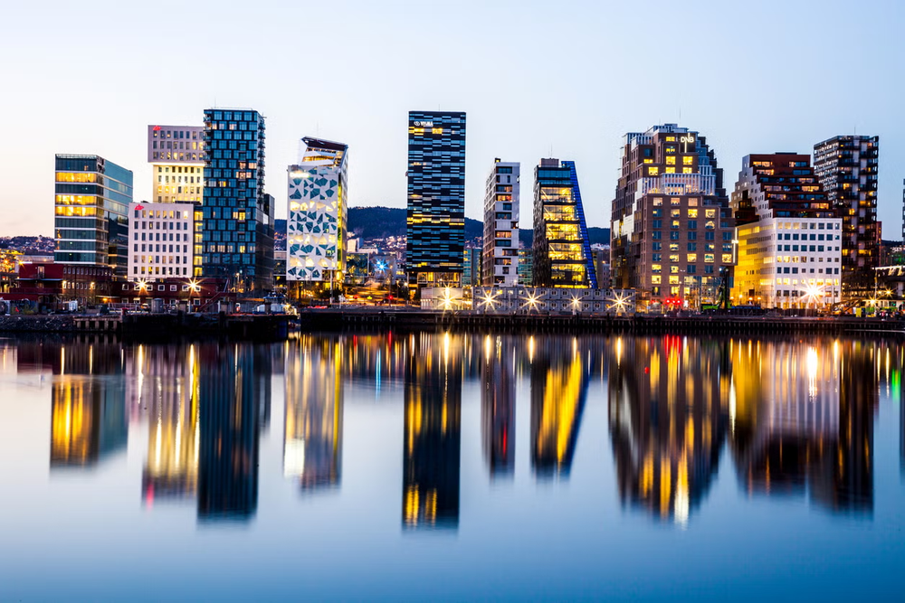 Modern skyline of Oslo reflected in calm waterfront at dusk.
