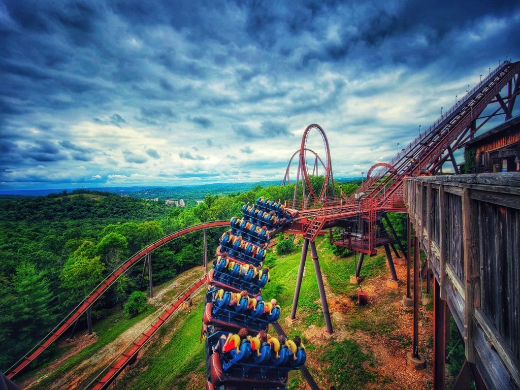 People riding a roller coaster with the Ozark mountains in the background on a cloudy day at Silver Dollar City in Branson, Missouri.
