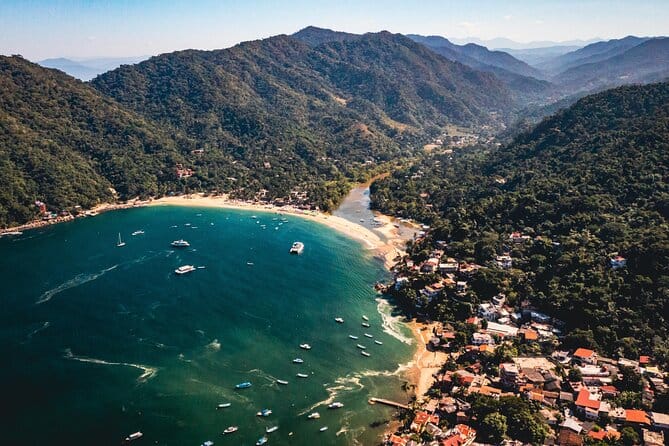 Aerial view of Yelapa, Mexico, showcasing a horseshoe-shaped bay with turquoise waters, boats anchored offshore, and dense green mountains surrounding the coastal village.