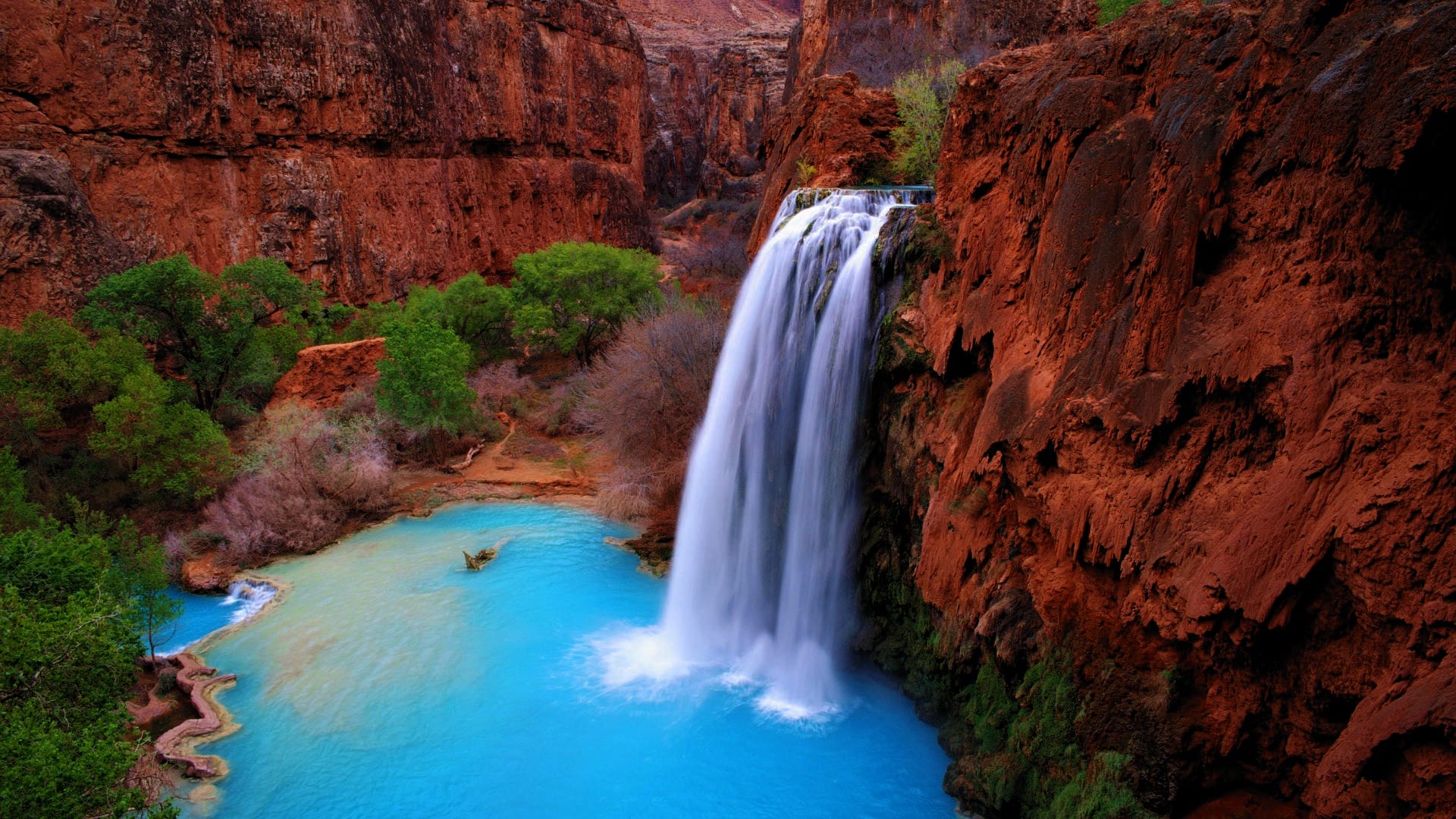 Havasu Falls spilling into a turquoise pool surrounded by red canyon walls in Arizona’s Havasupai Indian Reservation.