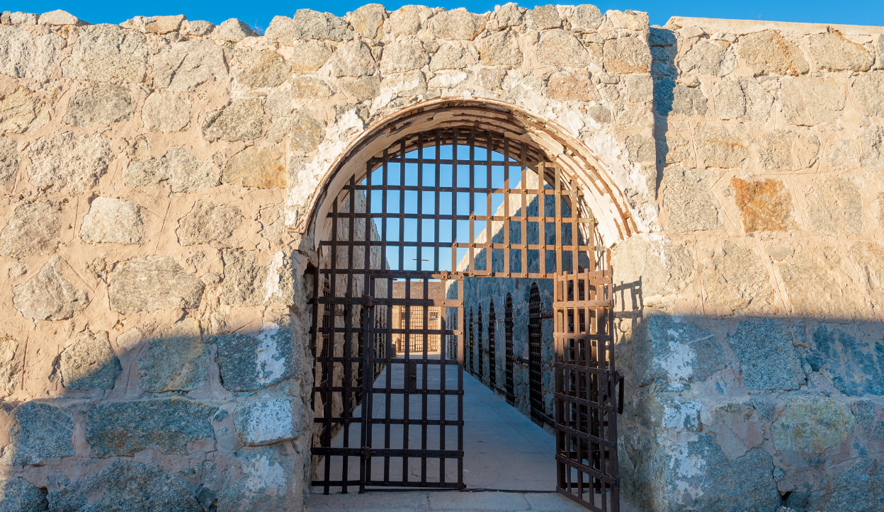 Entrance to an old rock walled prison with the metal gate entrance opened up for visiting to explore it at Yuma Territorial Prison State Historic Park.