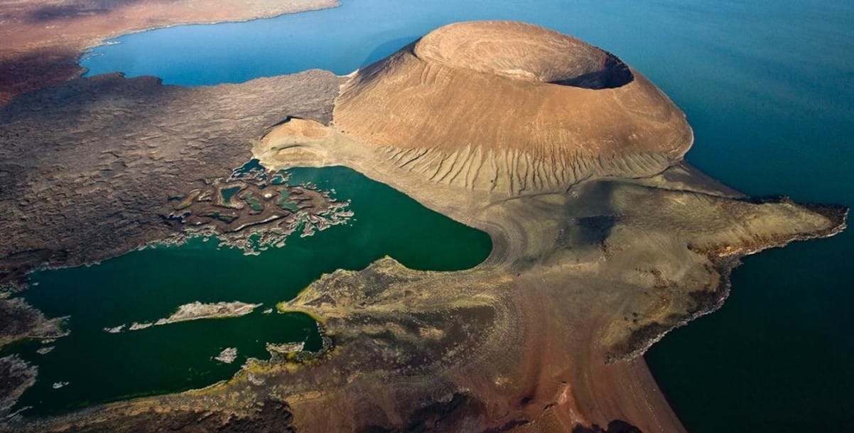 Aerial view of the volcanic island and turquoise waters of Lake Turkana, Kenya, showcasing dramatic geological formations.