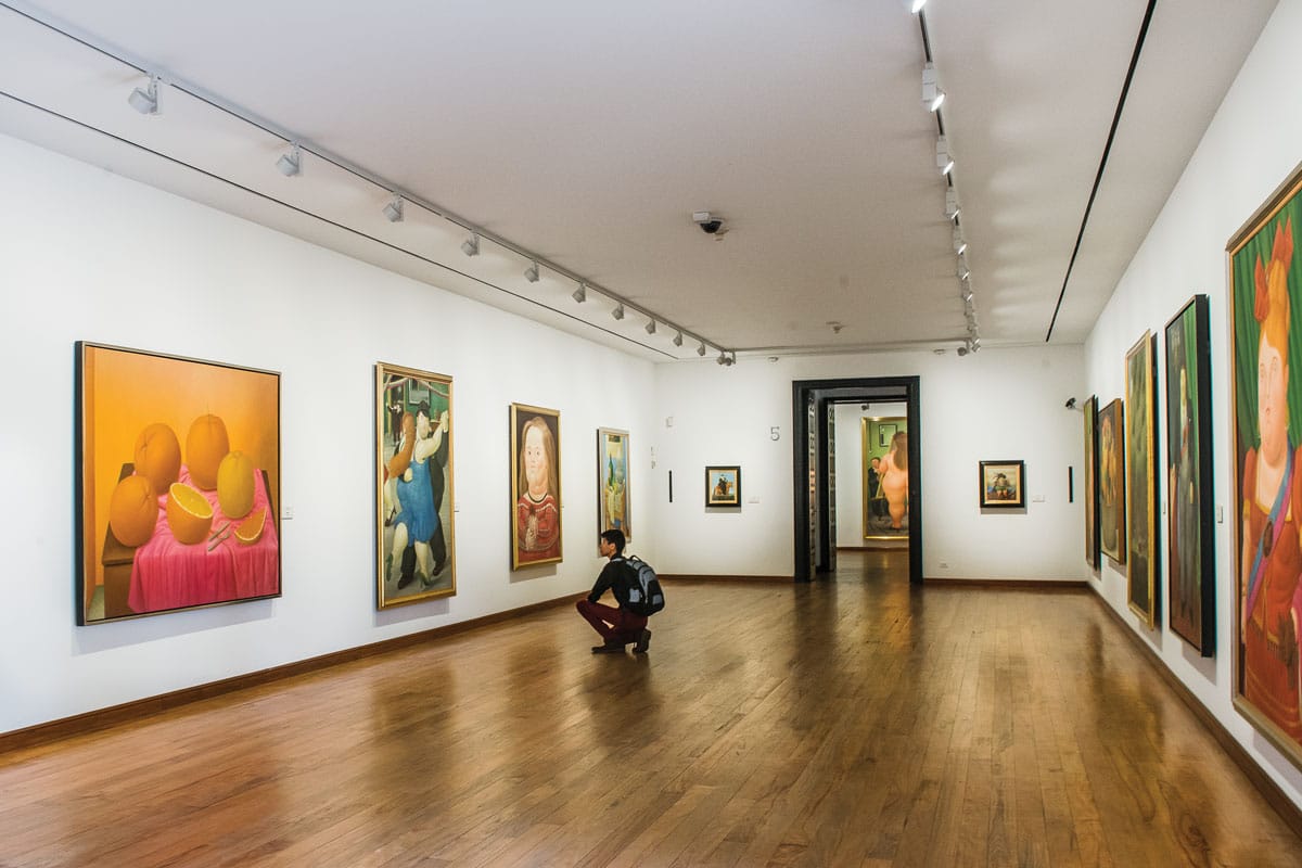 Art gallery interior at Museo Botero in Bogotá, Colombia, featuring colorful paintings by Fernando Botero and a visitor observing the artwork.