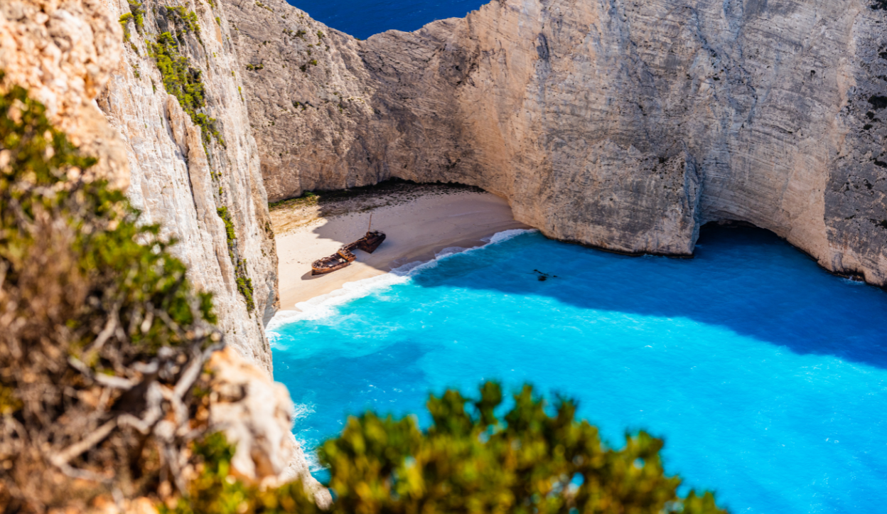 Aerial view of Navagio Beach (Shipwreck Beach) on Zakynthos Island, Greece, featuring a rusted shipwreck on white sands, surrounded by towering limestone cliffs and vibrant turquoise water.