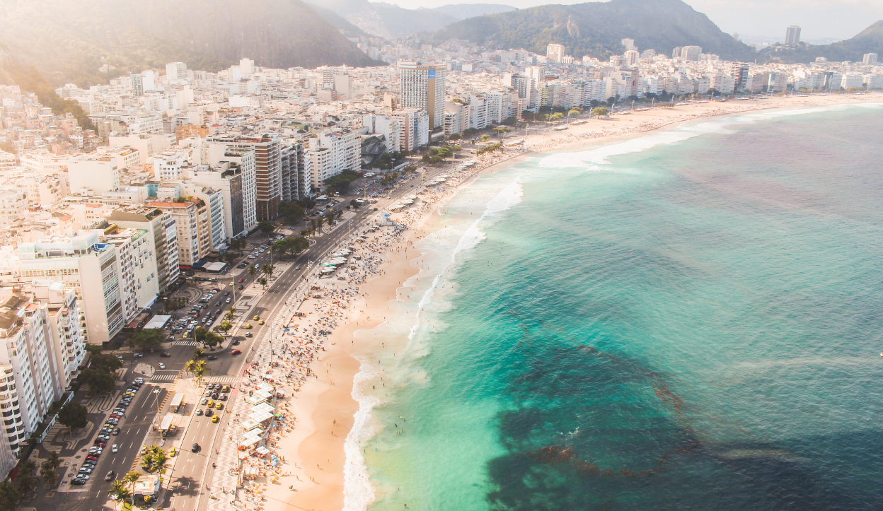 Aerial view of Praia de Boa Viagem beach in Brazil, showing turquoise ocean waves, high-rise buildings, and a busy coastal road.