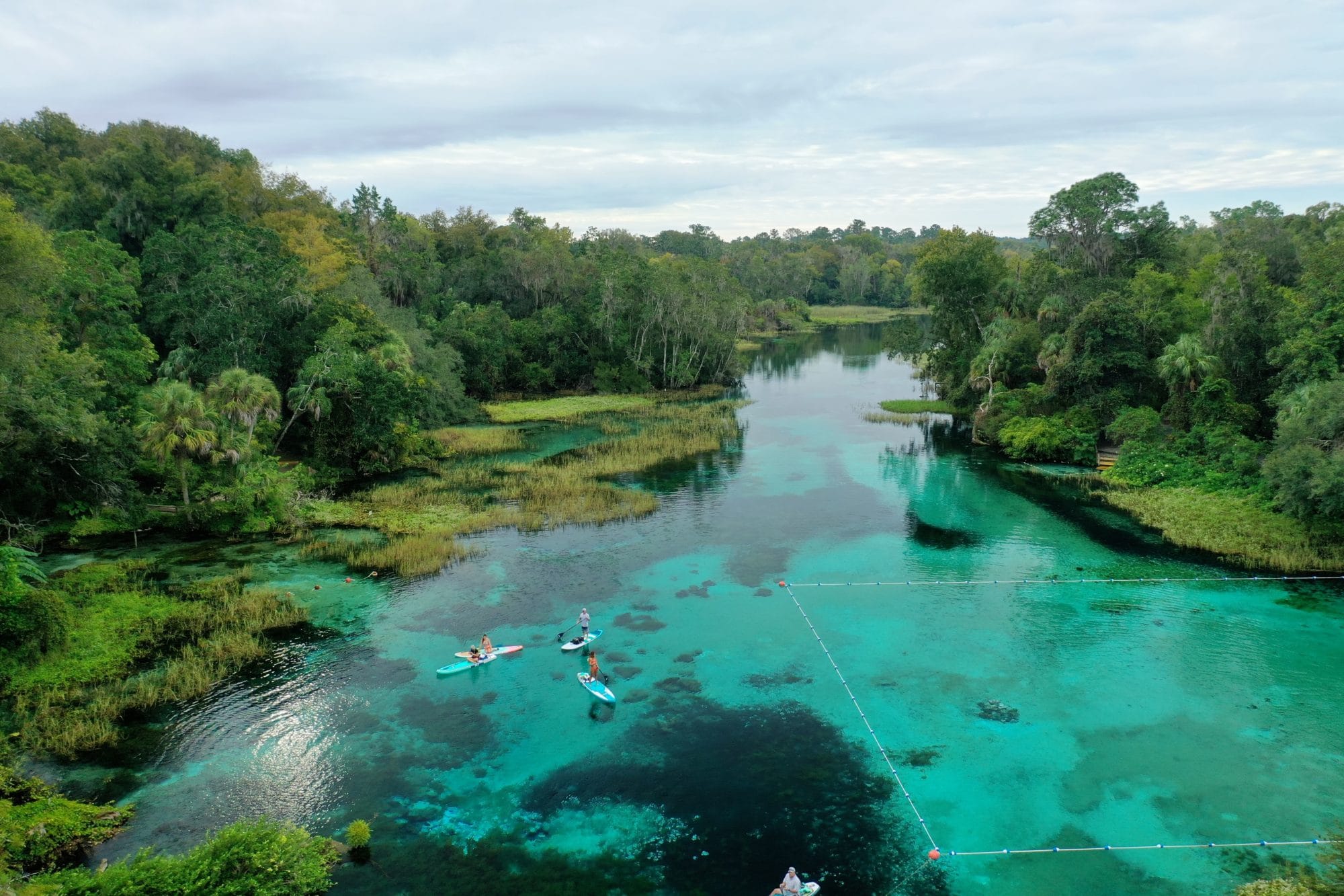 Aerial view of kayakers paddling over bright turquoise waters and lush green shoreline at Rainbow Springs State Park.