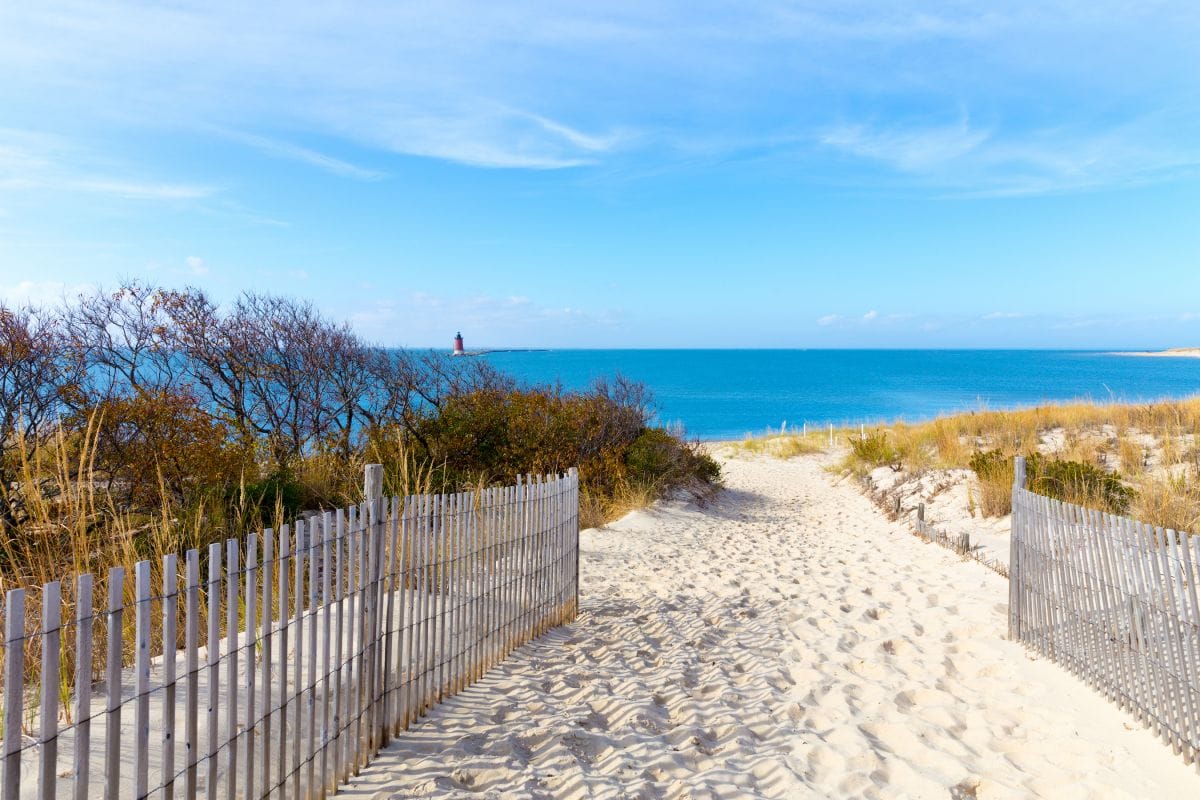 Wide sandy beach at Rehoboth Beach, Delaware, with ocean waves and coastal buildings in the background under a clear blue sky.