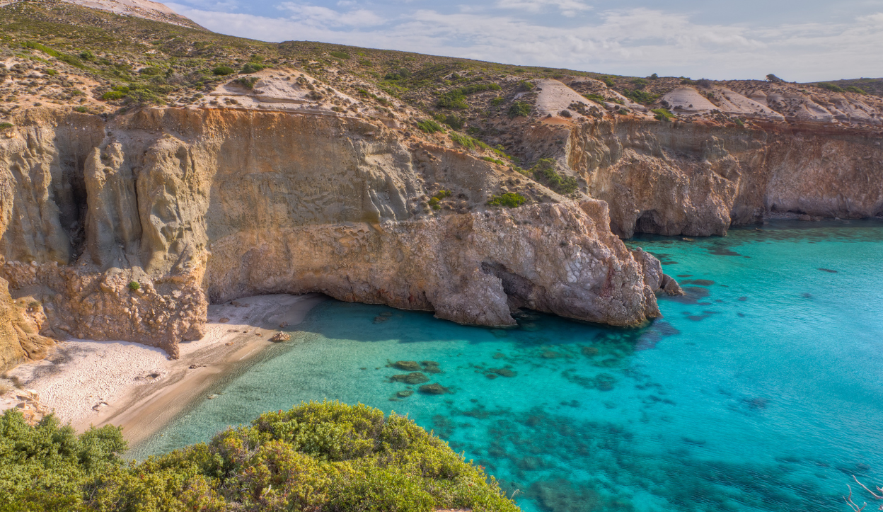 Secluded cove at Tsigrado Beach on Milos Island, Greece, surrounded by steep cliffs and featuring crystal-clear turquoise water and a narrow stretch of sand.