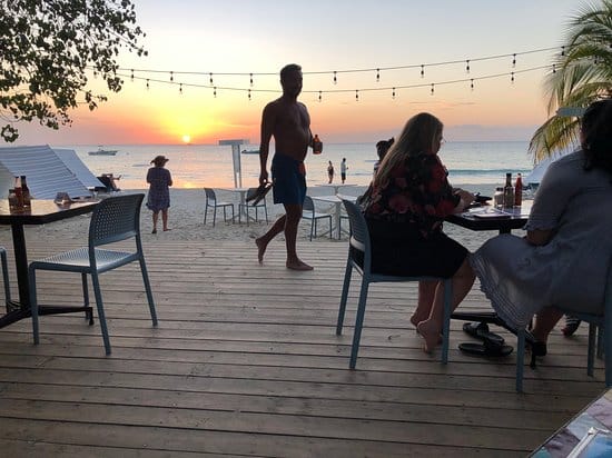 People sitting on a beachside patio enjoying drinks at sunset at Miss Lily's In Negril.