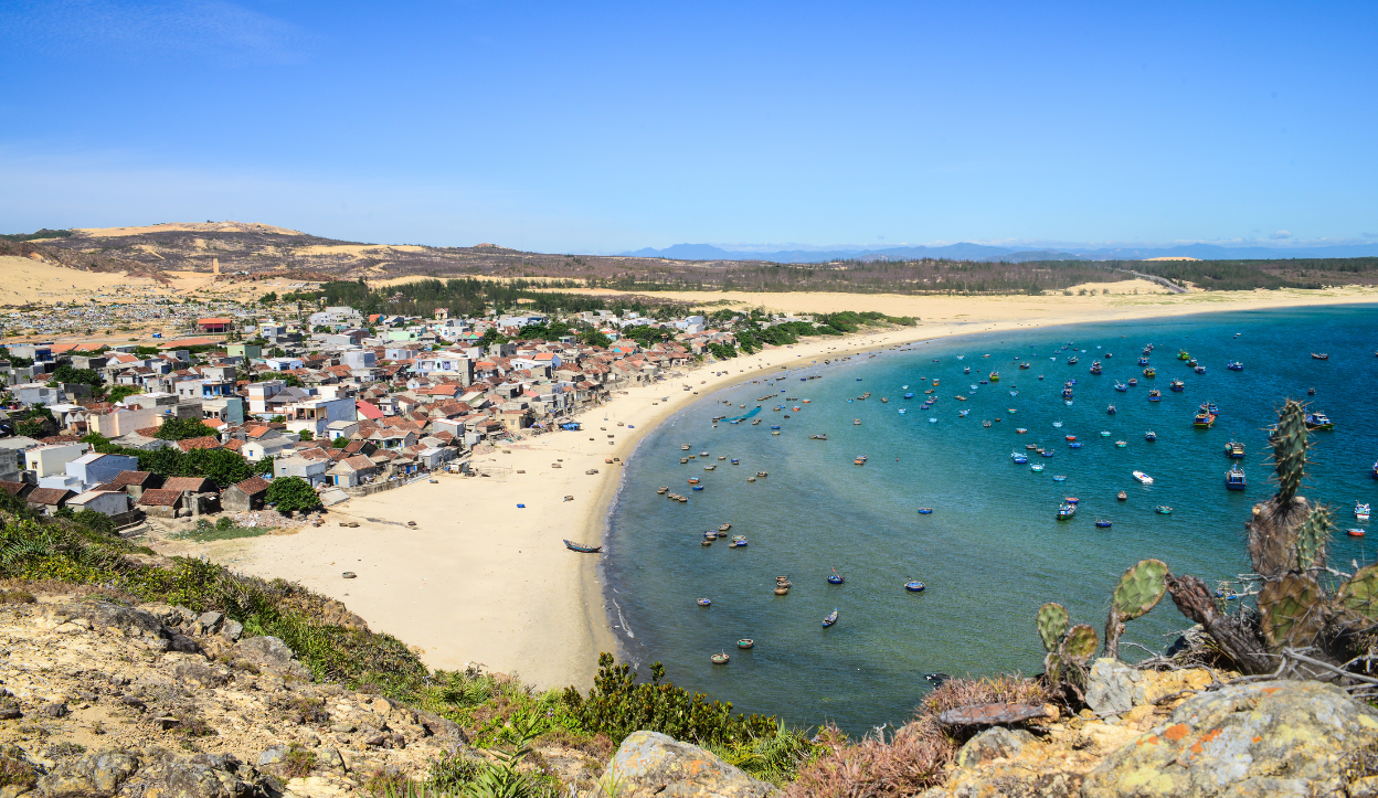 The seaside town of Quy Nhon, Vietnam with boats anchored in the water near the beach.