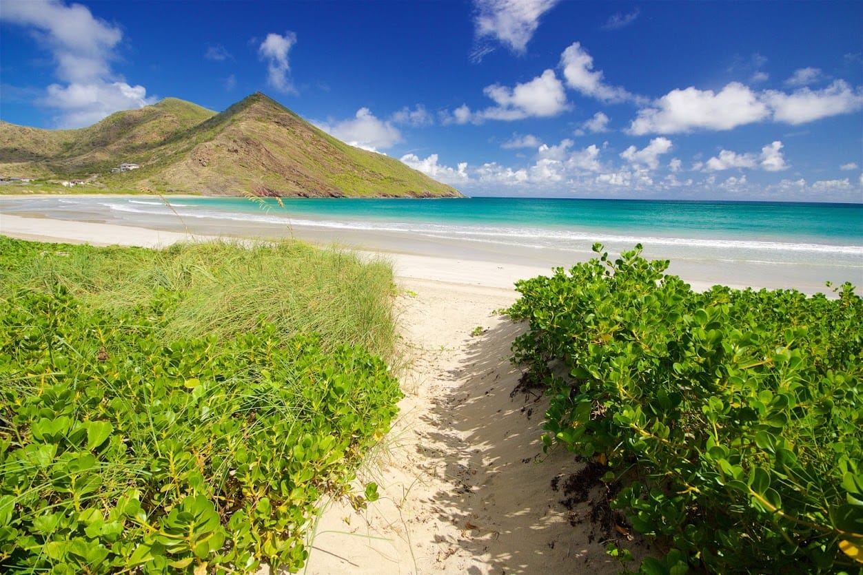 A sandy path to the beach at Sandy Bank Bay Beach in St. Kitts with clear blue waters and mountain views.