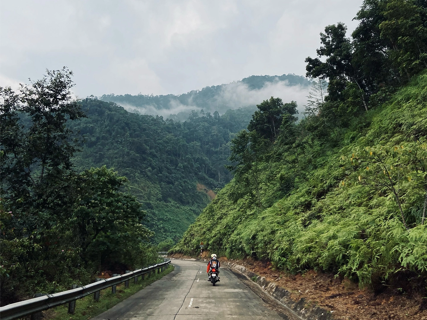 Going on a motor cycle on a road surrounded by mountainous jungle on the Ho chi minh trail