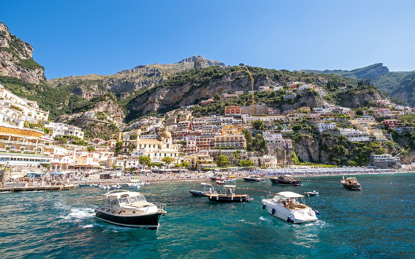 Boats anchored near mountains that have buildings over looking the seaside in the Amalfi Coast.