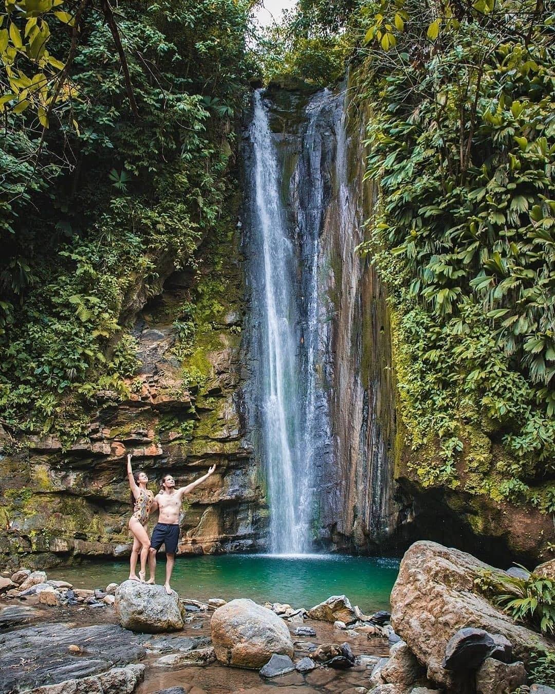 Two people pose for photo in front of the beatiful waterfall of Cascada del Tigre Quindio in Colombia.