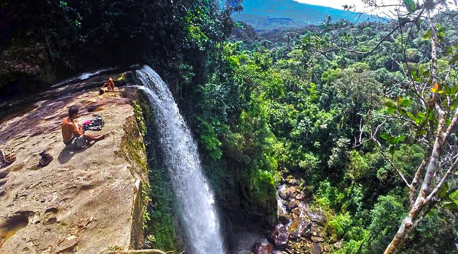 A man sitting at the top of a waterfall looking down at the cascading waterfall of Fin del mundo in Colombia.