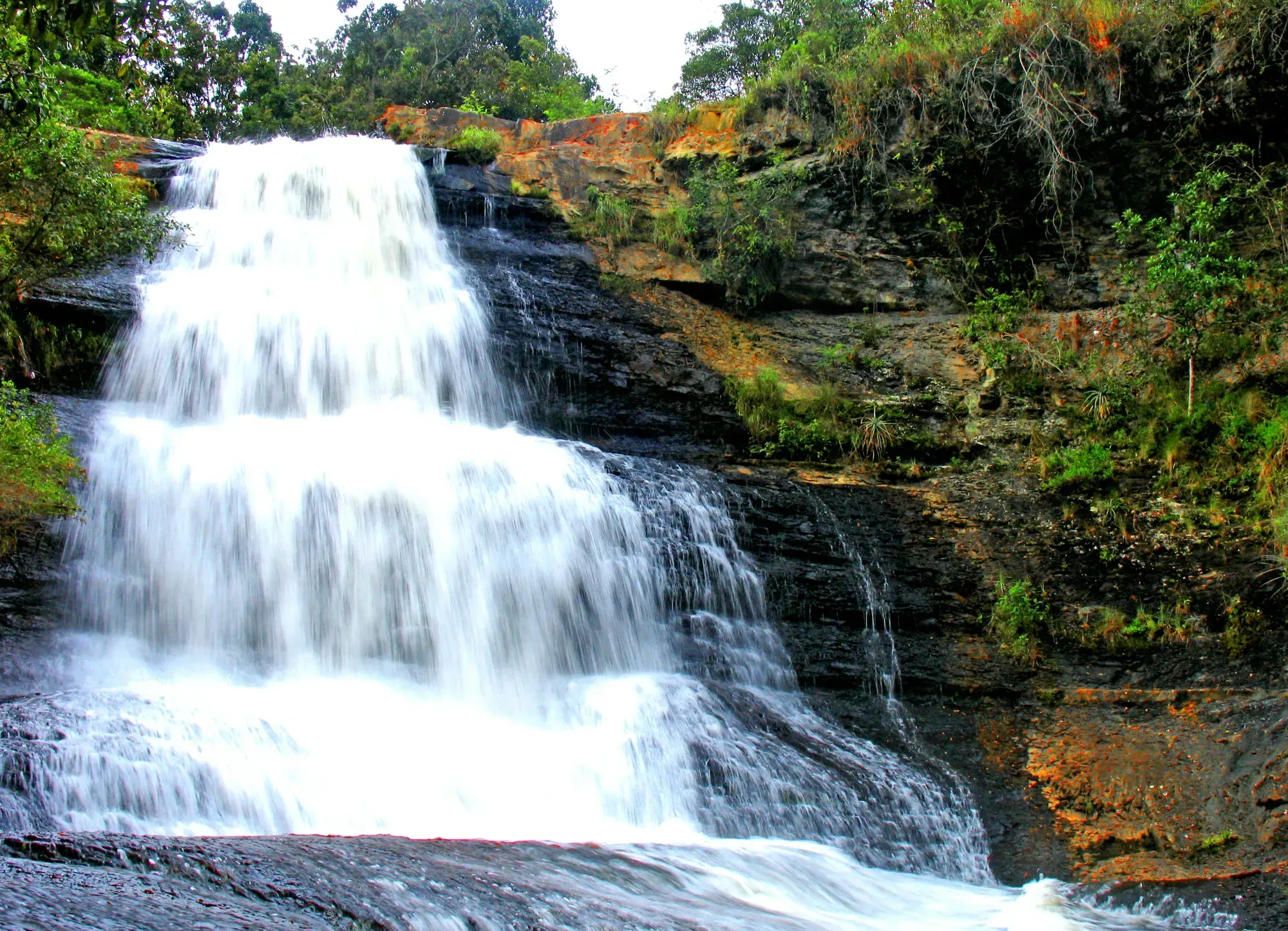 wide waterfall flowing down multiple levels of cliff like stairs at La Periquera waterfall in Colombia.