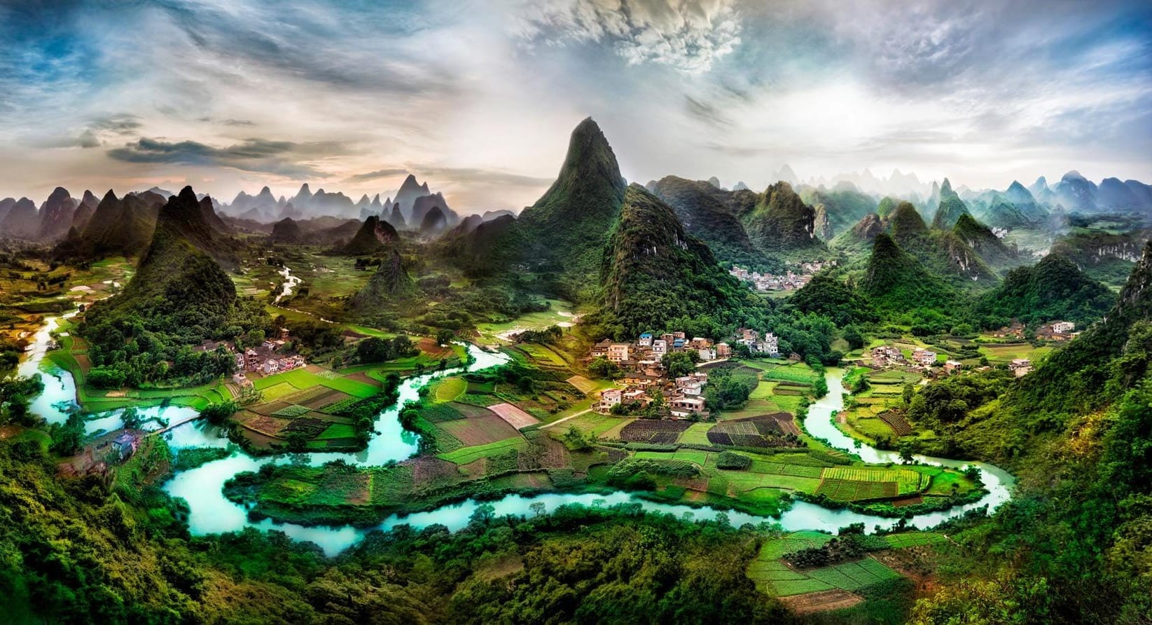 The most beautiful village with lush green grass with a river flowing through it surrounded by giant lush mountains in Cuiping Hill Village in Guilin, China.